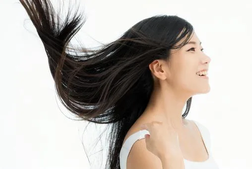 「風になびくツヤのある黒髪の女性が笑顔で振り向く様子｜サラサラ髪・美髪ケアの効果イメージ」