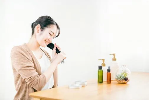 「ヘアオイルやケア用品を使って髪の毛を整える笑顔の女性｜自宅でできるナチュラルなヘアケアシーン」