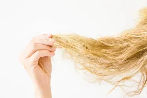 「パサつきや枝毛が目立つ傷んだ金髪の毛先を手で確認する女性｜ブリーチや乾燥によるダメージヘアの状態」