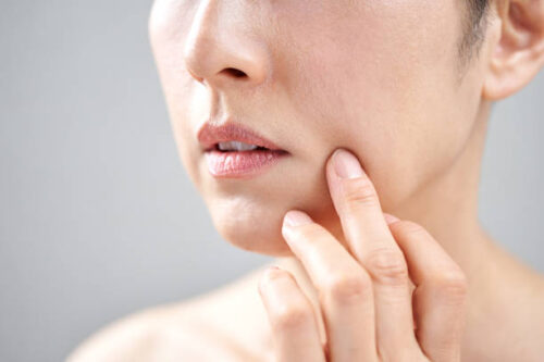 「肌のたるみやハリの低下が気になる女性が頬を指で押さえてスキンケアの必要性を確認している様子。エイジングケアやハリ対策に関連するイメージ」