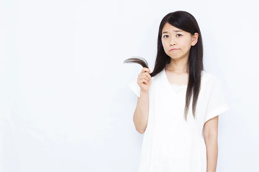 髪のうねりやパサつきに悩む女性｜毛先を見つめて困った表情をするストレートヘアの女性｜くせ毛・ダメージヘア対策イメージ