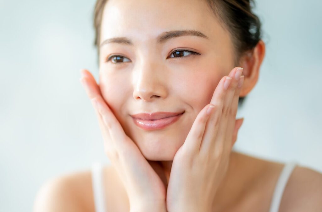 「スキンケア後の肌にうるおいとツヤを実感し、頬に手を添えて微笑む女性|化粧水や美容液の効果を実感する使用イメージ」
