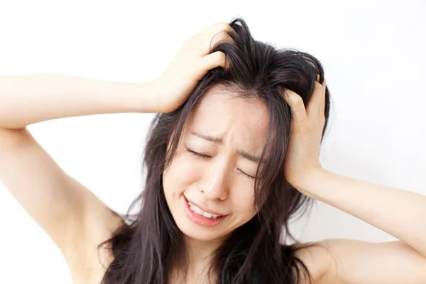 髪がまとまらず悩む女性が頭を抱える様子。くせ毛や広がる髪のスタイリングにストレスを感じているイメージ。