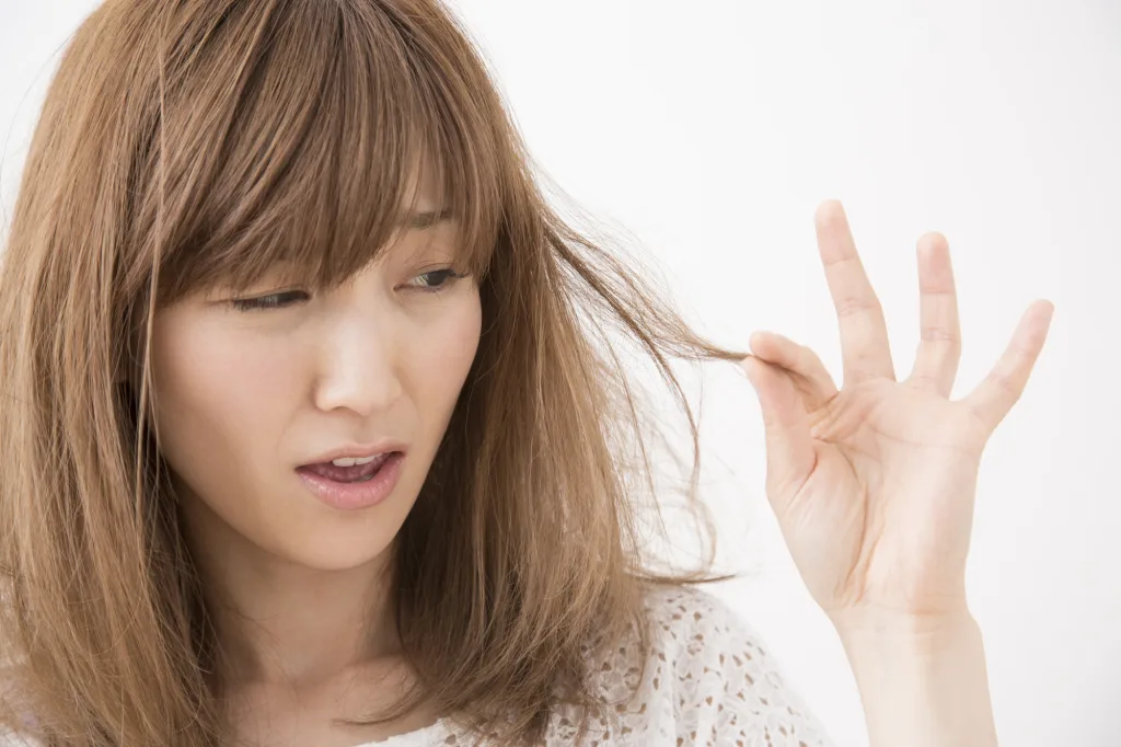 髪のパサつきやダメージに悩む女性が毛先をチェックしている様子|乾燥による広がり・枝毛・切れ毛などのヘアトラブルのイメージ