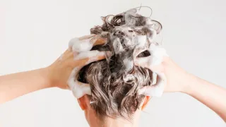 泡立てたシャンプーで頭皮と髪を丁寧に洗う女性の後ろ姿。シャンプー解析や正しい洗髪方法を解説する記事用イメージ